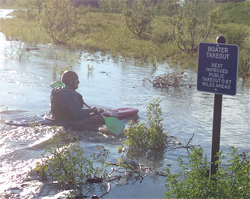 Kayaker next to boating takeout sign in creek