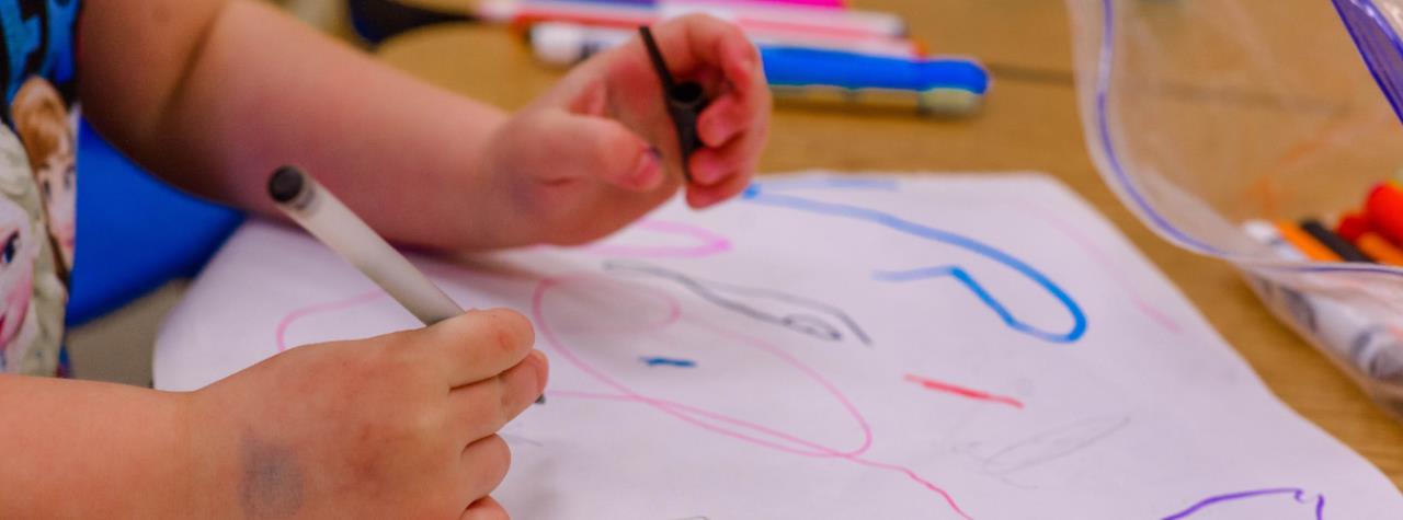 A child is creating a brightly-colored drawing with markers