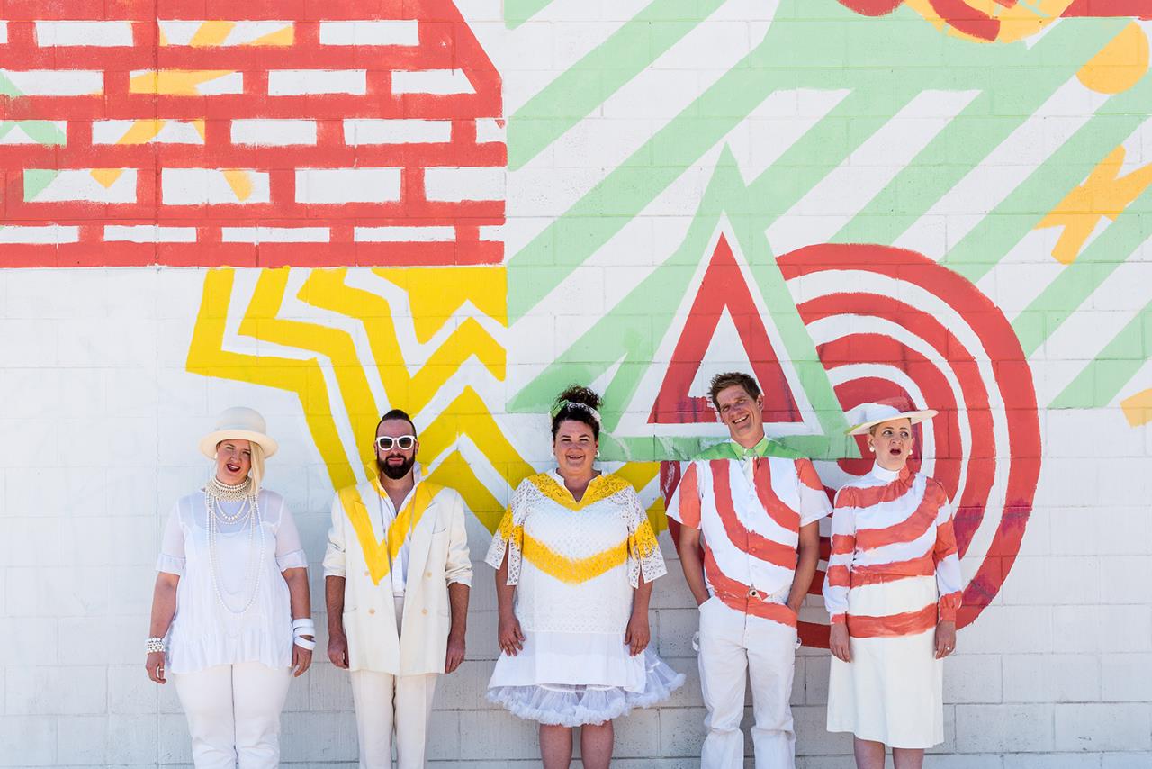 Photograph of Buntport Theater in front of colorful wall with line patterns painted on their clothing to match wall