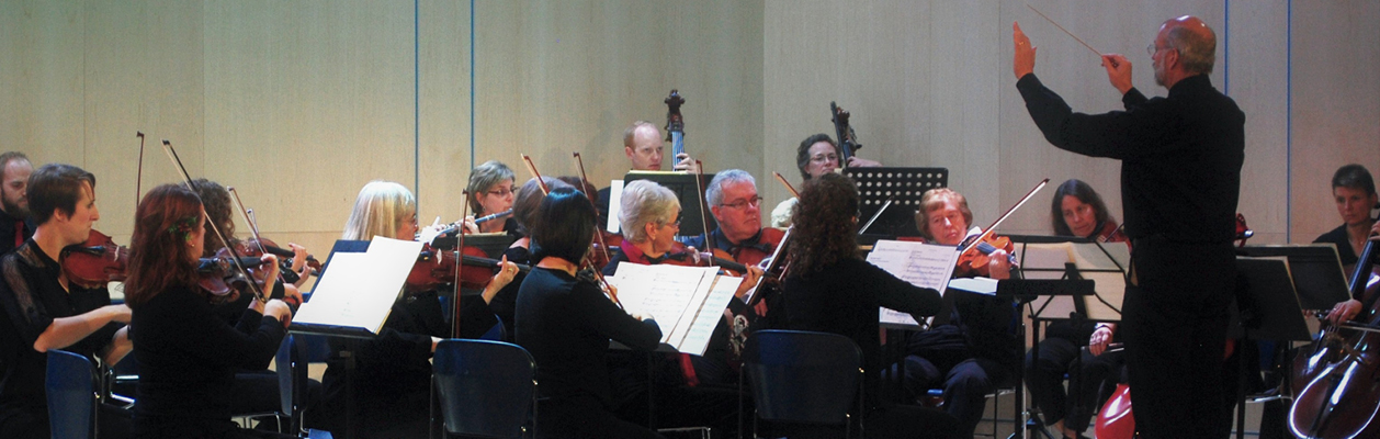 A conductor leads an orchestra on stage at the Longmont Museum