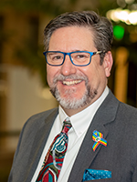 Longmont City Council member Sean McCoy poses for a portrait wearing a white button down, gray suit jacket and patterned red tie