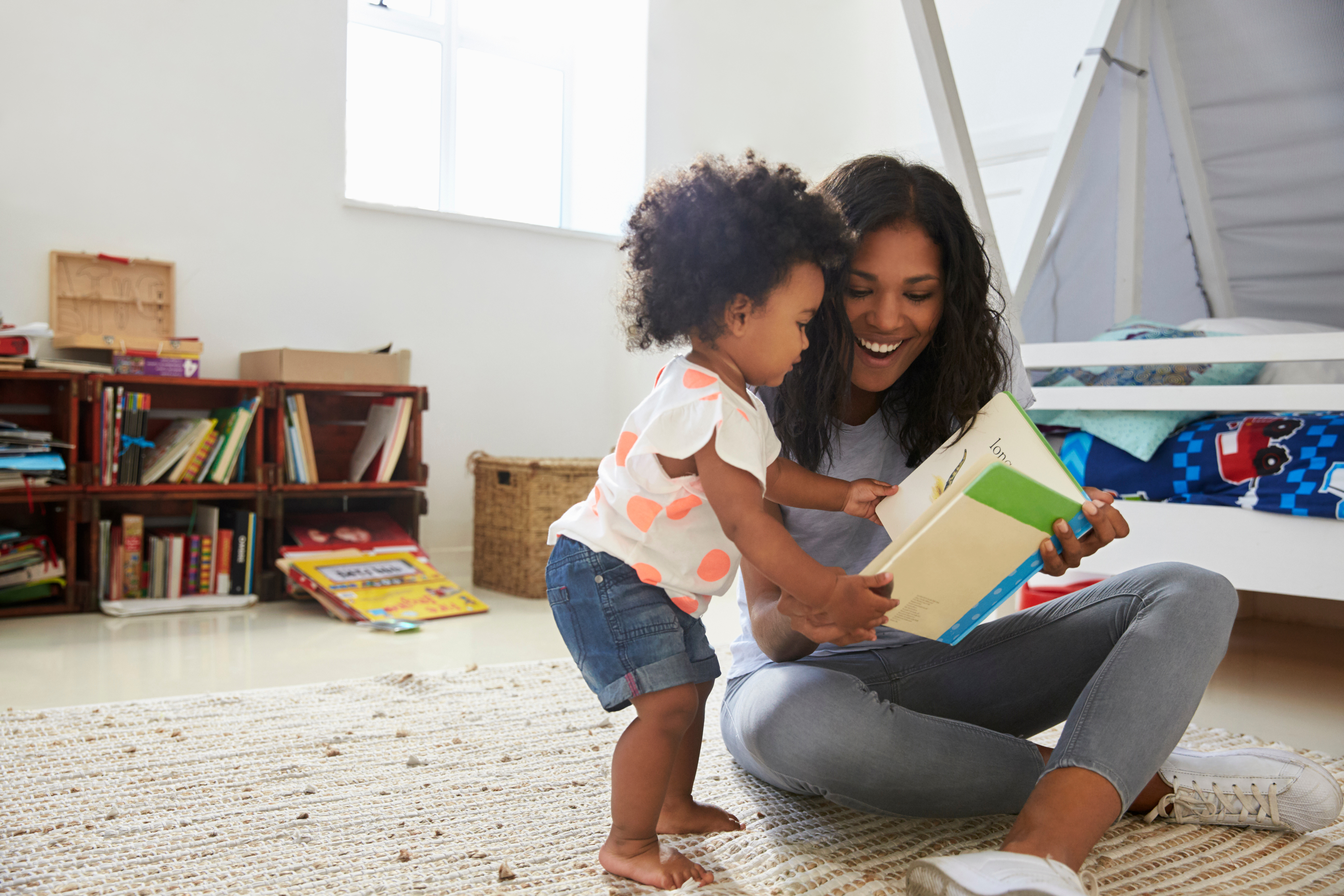 Mother And Baby Daughter Reading Book In Playroom Together