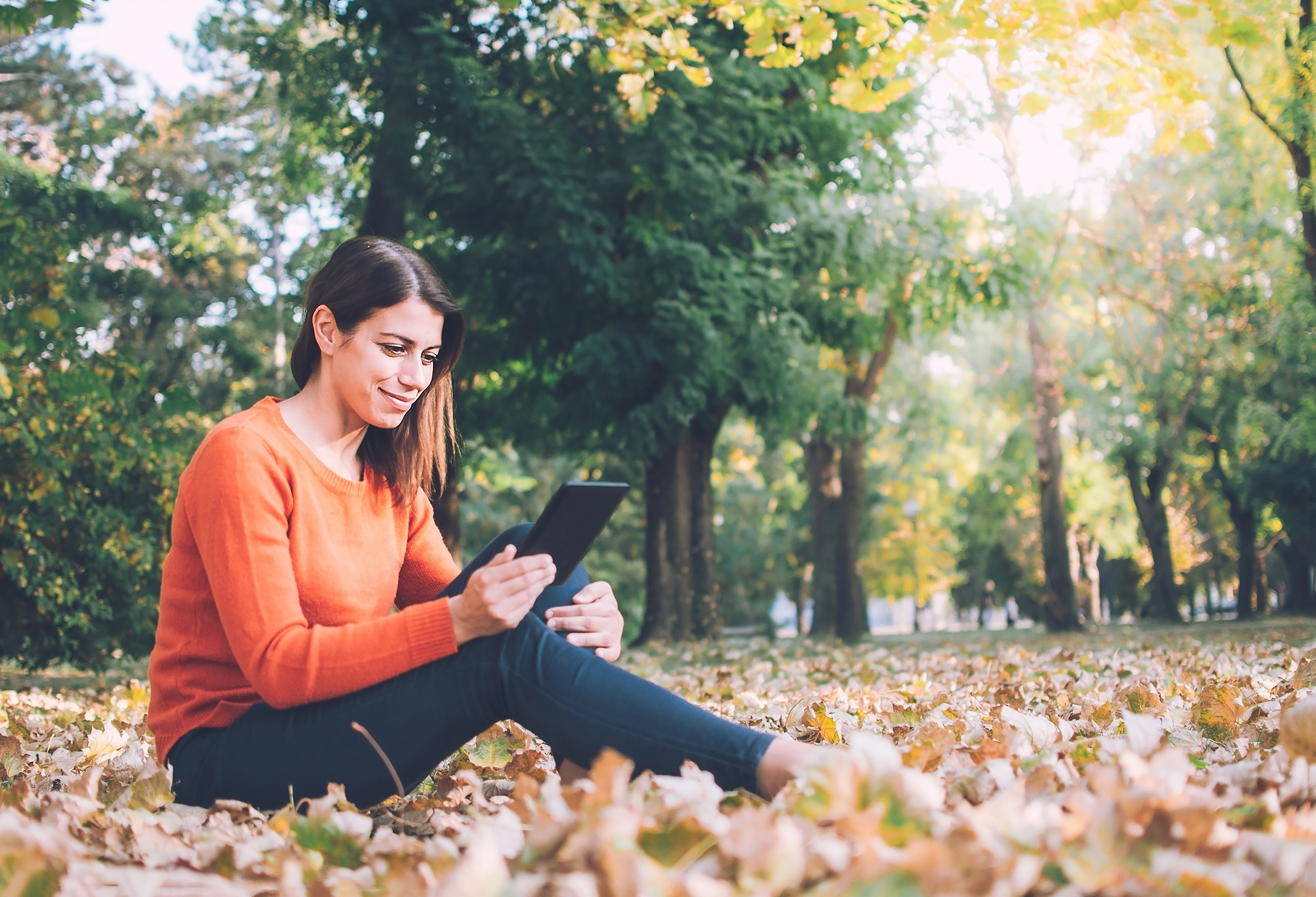 A woman reads on her tablet outside during the fall