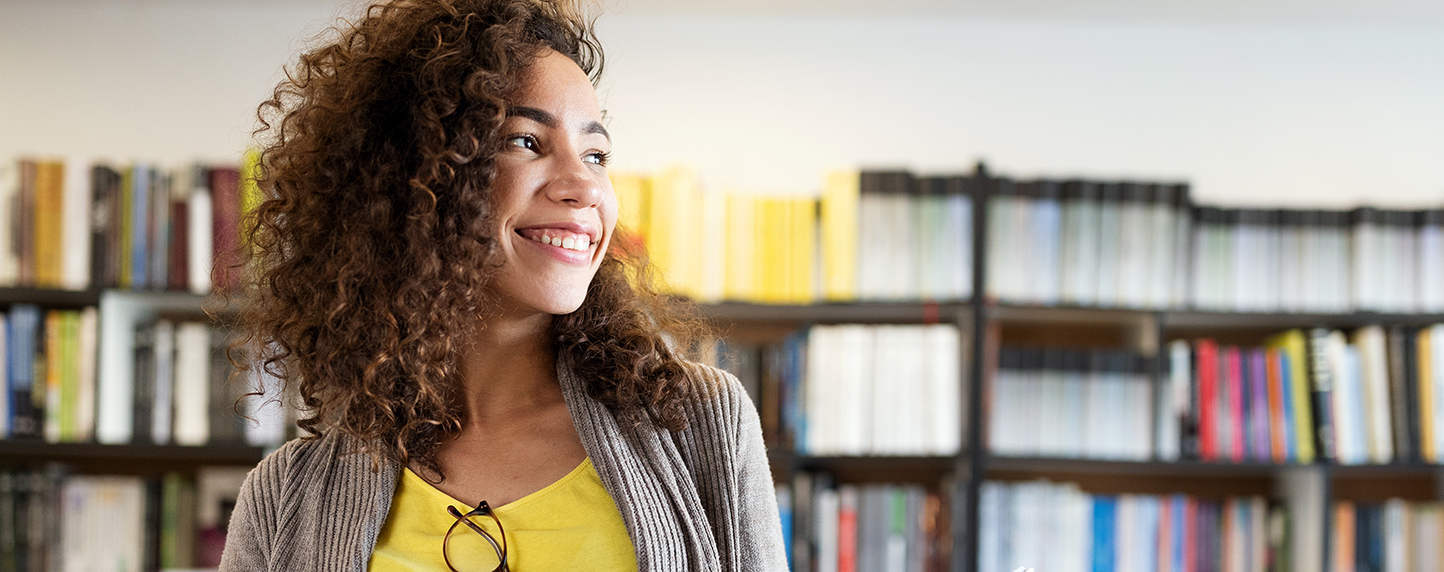 Smiling happy student girl reading book at library