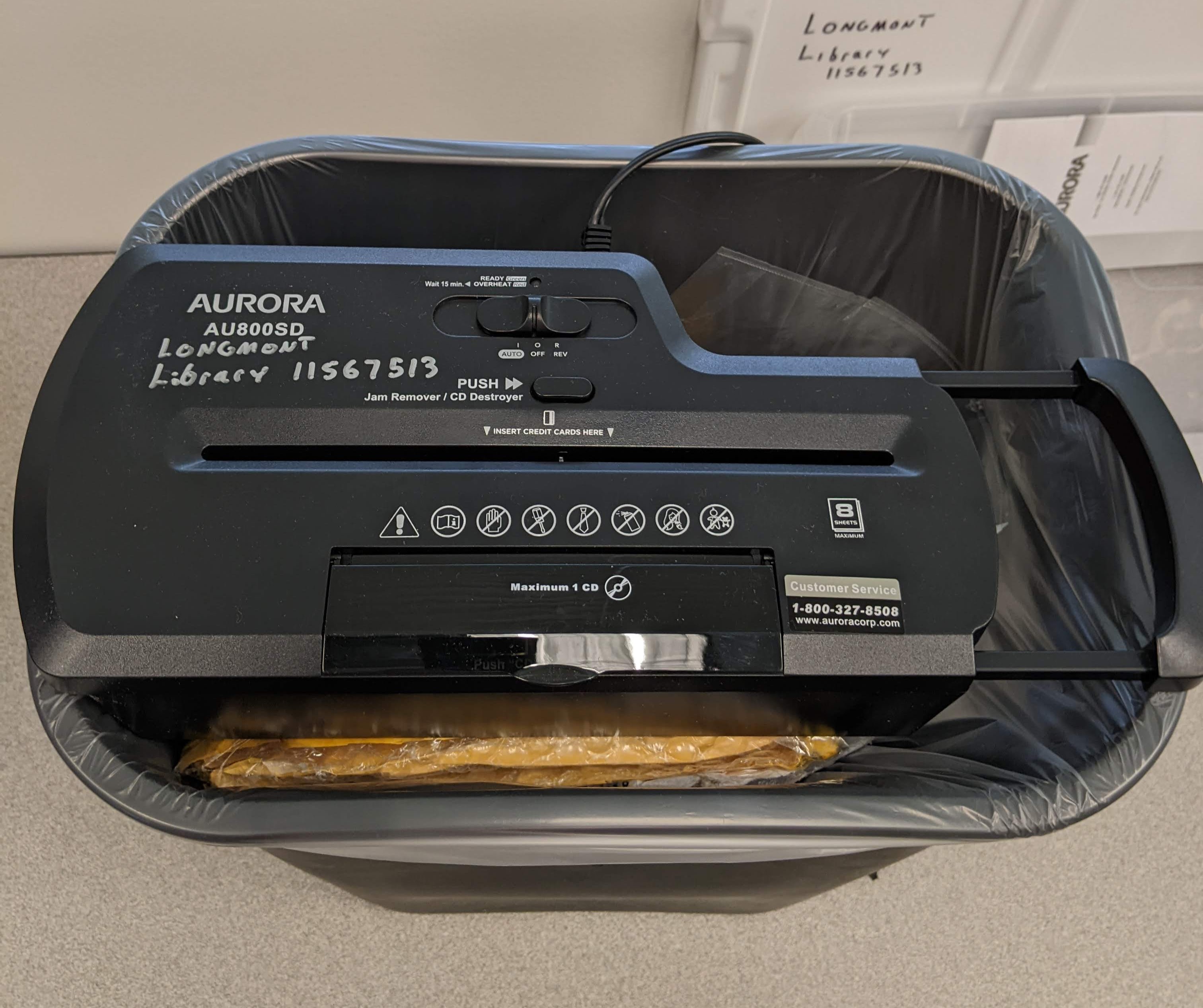 A portable paper shredder sits on the top of a small trash can