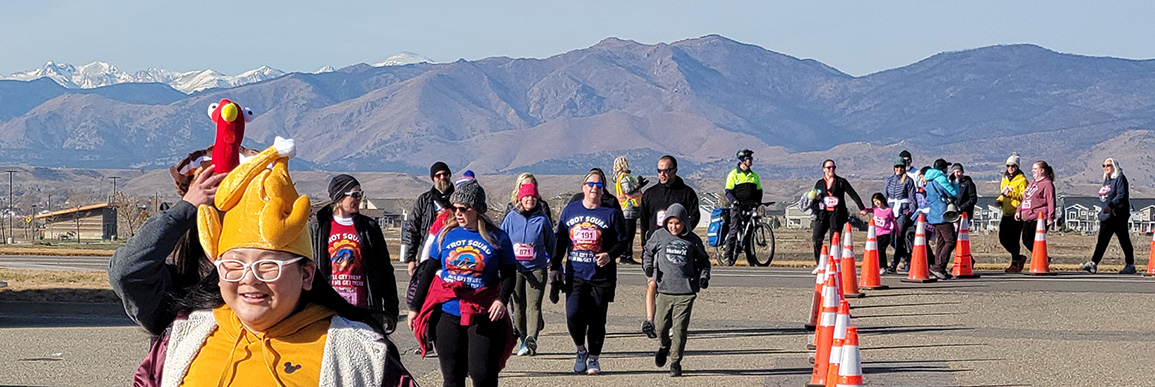 Girl with turkey hat with other racers in the background and a mountain range showing behind.