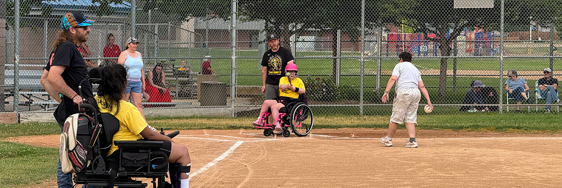 A unified softball player in a wheelchair prepares for the pitch.