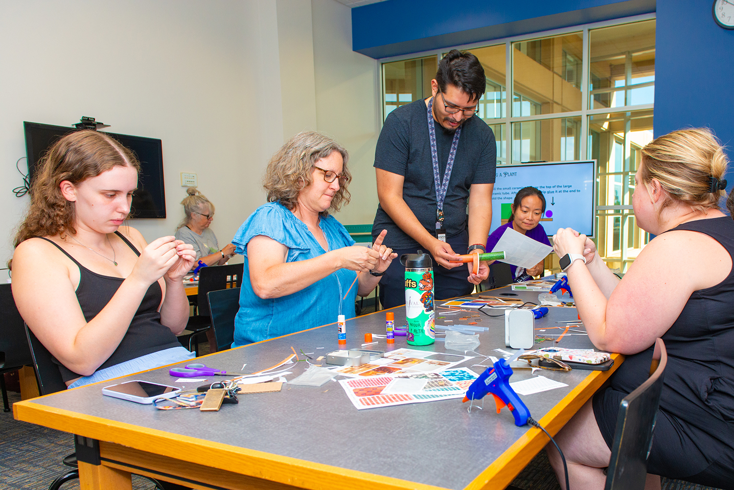 A group of people sit around a table making a craft at the Library