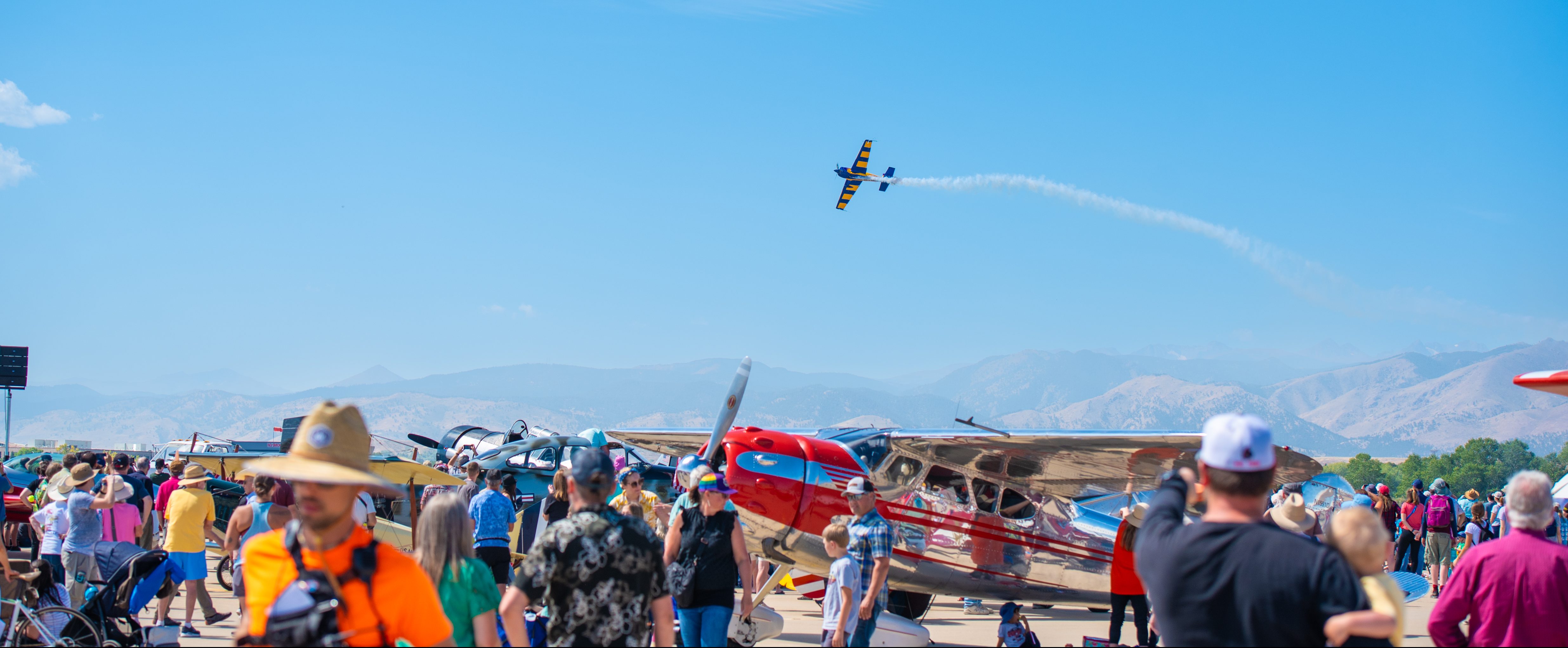 Crowd watching a plane flying through a blue sky with a view of the mountains from Vance Brand Municipal Airport